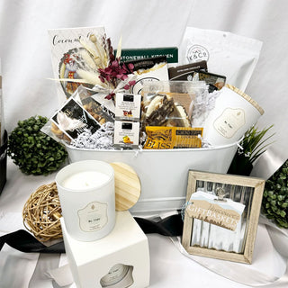 Gift basket with various items including a candle, snacks, and a photo frame on a white surface.