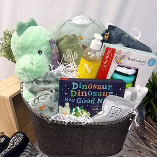 Gift basket with baby items including a plush dinosaur, baby clothes, and a book titled 'Dinosaur, Dinosaur Say Good N'.