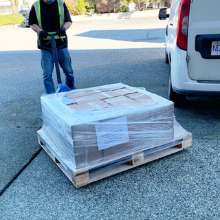 Person loading a pallet of gift boxes onto a white van in a driveway.