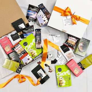 Assorted food products including chocolate bars and snacks on a white surface with orange ribbons.