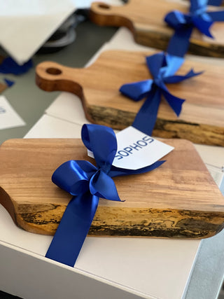 Wooden cutting boards with blue ribbons and a visible brand name on a surface.