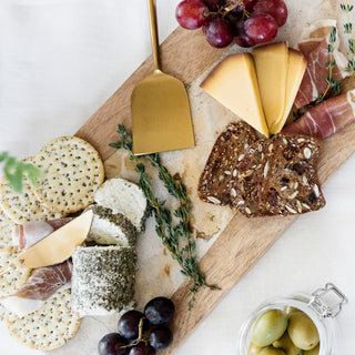 Assorted cheeses, meats, and crackers on a wooden board with grapes and olives.