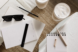 Notebooks, sunglasses, and a pen on a textured surface with two cups of coffee.